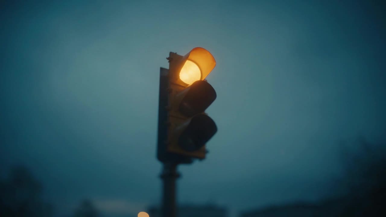 A single amber traffic light glowing in soft blue dusk.